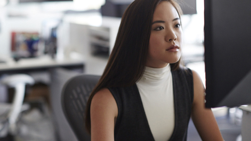 Woman at desk looking at computer monitor.